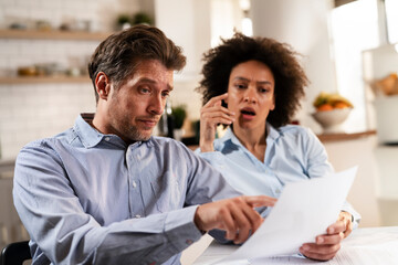 Young couple sitting in the kitchen preparing bills to pay. Stressed woman and man having financial problems.