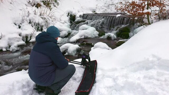 A man uses a slider camera to film a beautiful stream in a winter forest in the Carpathians