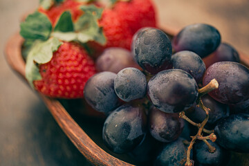 Delicious fruits on a wooden table. Strawberries and grapes. Close up.