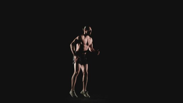 Athletic man jumps high on the spot on a black background. Slow motion