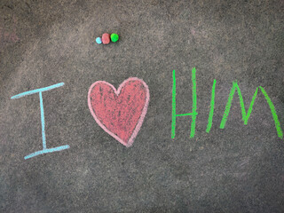 The inscription text on the grey board, I with hand drawn love symbol and him . (I love him). Using color chalk pieces.