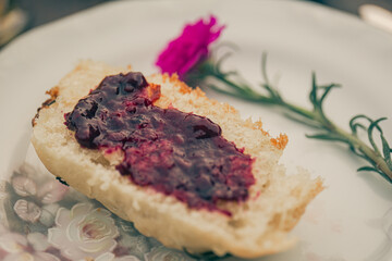 Slice of bread with strawberry jam and a flower in a white plate. Top view.