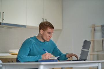 Entrepreneur man on the phone working with a laptop in the kitchen at home. freelancer is negotiating on a smartphone