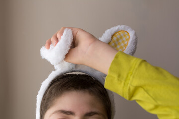 Boy trying to take off furry bunny ears headband; Easter with a child with Autism