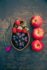 Delicious fruits on a wooden table. Strawberries, grapes and apples. Space for text. Top view.