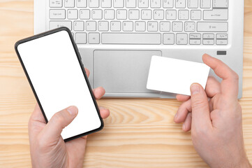 Mockup image. Online Shopping And E-Payments. man hands hold cell phone with blank white screen and mockup credit card on lapto background. top view