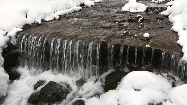 A mountain cold little stream flows among stones and trees in the snow-capped mountains of the Carpathians, 3x slow-mo