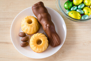 Easter sweets on white plates on a wooden table. Chocolate bunny, eggs and Easter muffins.