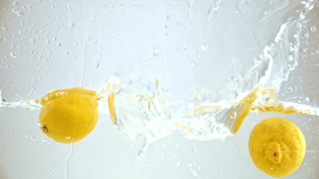 yellow ripe lemons falling in water on white