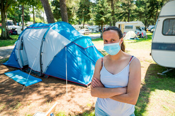 Woman wearing medical mask standing in front of a camping tent in resort.