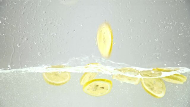 sliced juicy lemons falling in water on grey