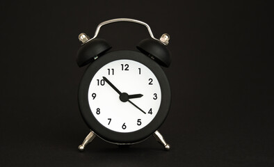 black alarm clock with hands on black background
