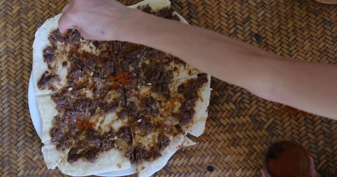 Close up of a hand putting spices on Manakish Lahm Bi Ajeen - Flatbreads with minced lamb or beef and Fatayer stuffed pie with spinach. Traditional Arab food