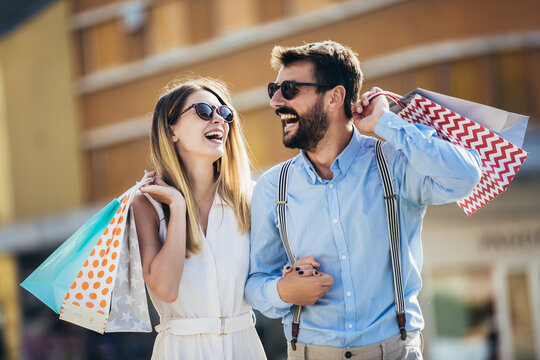 Happy young couple with shopping bags after shopping in city smiling and huging