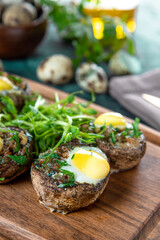 Baked champignons with quail eggs and microgreen garnish on a wooden cutting board, close up vertical photo