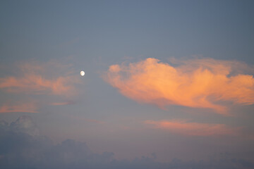 Blue sky and orange clouds. Sunset sky with the moon, the clouds are colored in orange.