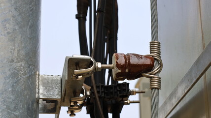 Earth wire on insulators next to metal poles. Short circuit protection or lightning protection system for mobile phone substation of 4G or 5G wireless type. Close focus and select an object.
