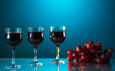 Pouring red wine into the glass against blue background and grape