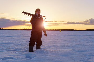Fototapeta premium winter fishing. Young man fisherman with a drill for ice fishing. sunrise