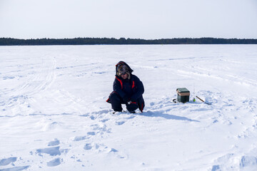 fisherman fishing on a winter lake against a background of forest and blue sky. winter fishing