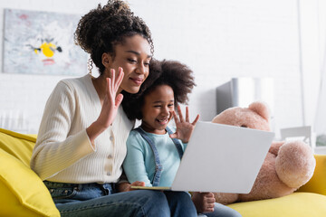 smiling african american mom and child waving hands during video chat on laptop