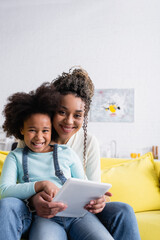 happy african american woman with daughter looking at camera while using digital tablet