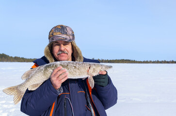 adult male fisherman with a pike catch on a winter lake. Winter fishing