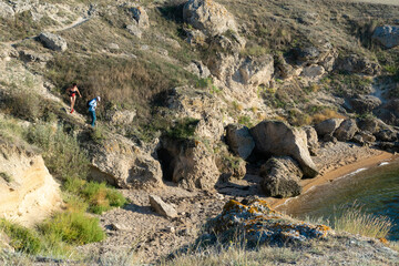 tourists descend a steep rocky path to a secluded sandy beach on the shore of the Sea of Azov in...