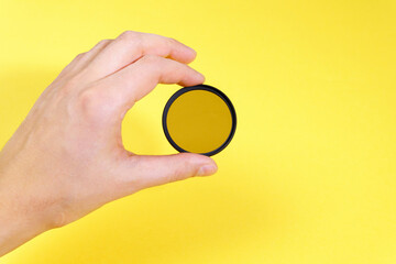 man hand holds a circular polarizer filter, on yellow background. photo accessory