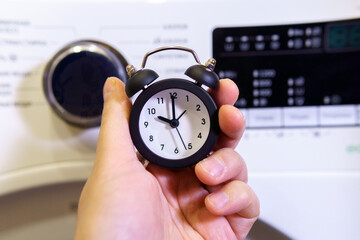Washing clothes, alarm clock in hand selective focus.