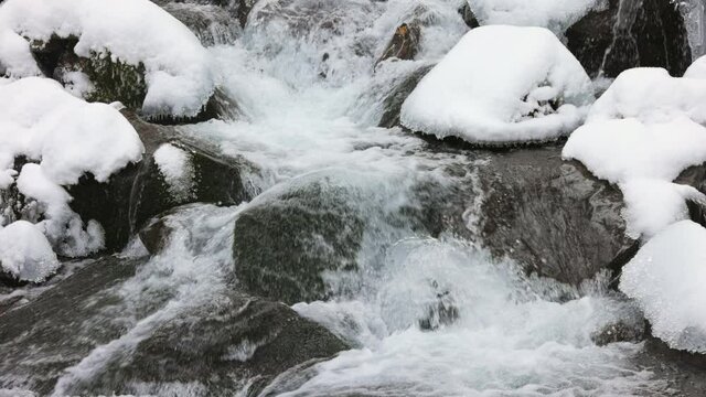 Small mountain streams of icy water flow among wet stones covered with white snow, and 3x slow-mo