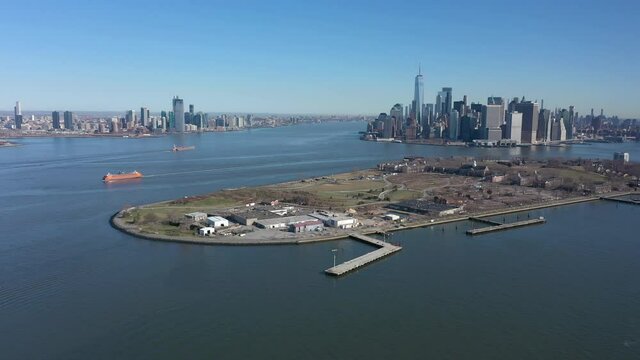 An aerial view over New York harbor on a sunny day with blue skies. The camera dolly right with Governor's Island in view and showing NJ and lower Manhattan in the background.