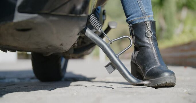 Close-up of woman's black boot pushing the scooter off of the stand. Slow motion.