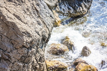 Turquoise sea stone beach, breaking waves in bright sunlight. Colorful bright sea background. The concept of summer, vacation, travel. The purest sea water, large stones on the beach close-up