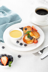 Cottage cheese pancakes, syrniki, with honey and berries in a white plate and black coffee, horizontal view, restaurant serving, breakfast