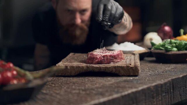 Chef cook preparing piece of meat. Spinkle a lot of salt on it. Slowmotion.