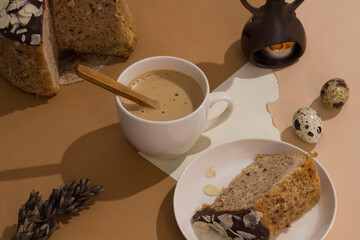 A cup of latte on a sandy beige background with a tough shade with exquisite chocolate Easter cake and quail eggs. Easter holiday card minimalism. Trendy isometric beige background. Creative postcard.