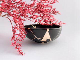 Black Kintsugi bowl with pink flowers, Japanese restoration technique with gold scars, the beauty...