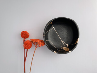 Black Kintsugi bowl with red flowers, Japanese restoration technique with gold scars, the beauty of imperfection