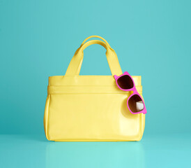 Yellow handbag purse with pink sunglasses isolated on blue background. 
