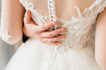 Obraz na płótnie Canvas Female hands dress the wedding dress on the bride. Morning of the bride, preparation for the wedding.