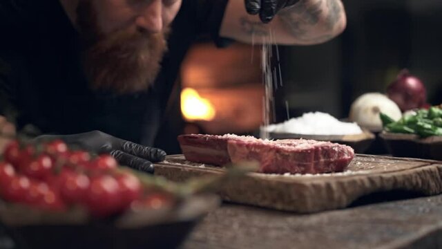 Close-up. Cook man spinkle salt on the steak. Slowmotion.