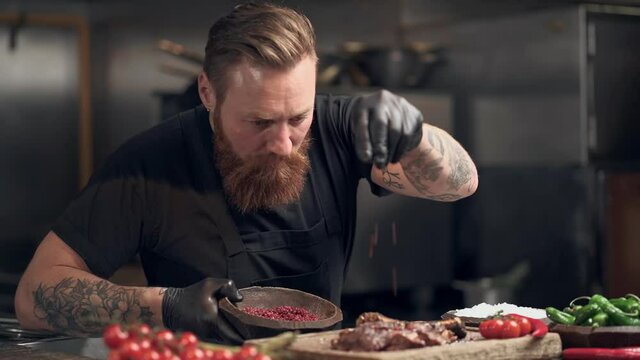 Cook man sprinkle red pepper on the meat. Slowmotion.