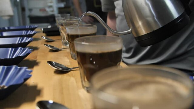 Hot steamy water is poured for coffee cupping taste test, slow motion close up