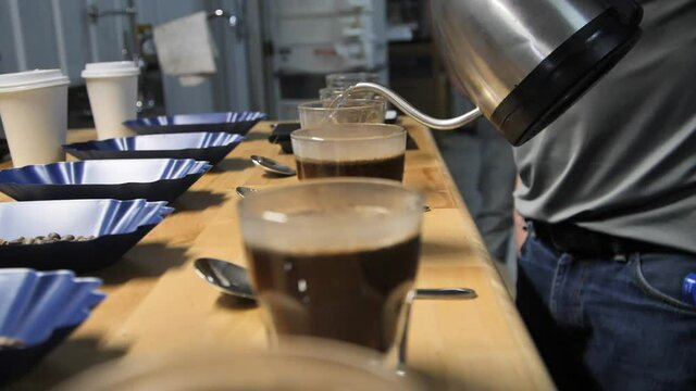 Man pours hot water for coffee cupping taste test, slow motion close up