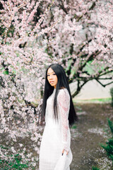 portrait of beautiful young asian woman with blooming cherry blossoms sakura flowers. Enjoying of spring. flying petals of cherry