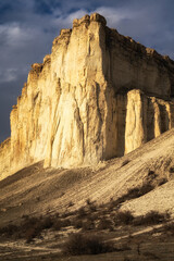 Beautiful white mountain peak lit by sun. White clouds and blue sky on background. Epic rock formation