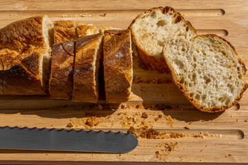 Delicious fresh baked baguette cut on a wooden cutting board with bread knife