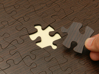 Hand holds last missing piece of wooden puzzle 