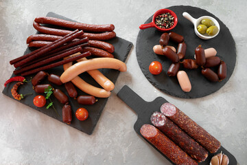 Smoked, boiled, hunting sausages of different sizes lie on slate boards with tomatoes, dried pepper, garlic, a sprig of parsley, with saucers with colorful peas-peppers and olives. Top view..